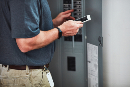 a man holding a tablet while checking an electrical panel