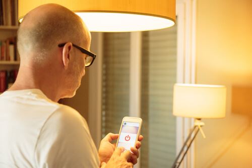 Man using smart phone to turn on lights in his home 